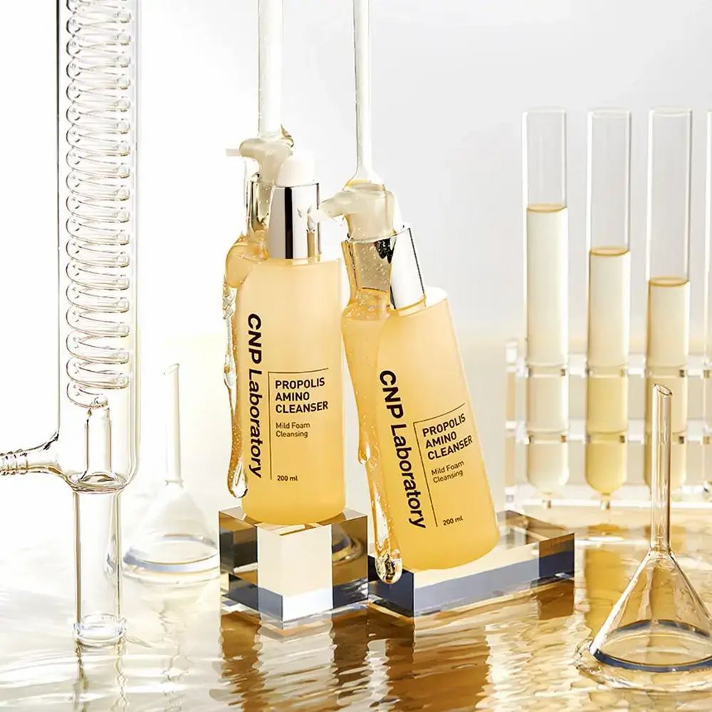 Twee gele flessen met pomp. Opschrift: CNP Laboratory, Propolis Amino Cleanser, Mild Foam Cleansing. 200 ml. Laboratorium achtergrond.