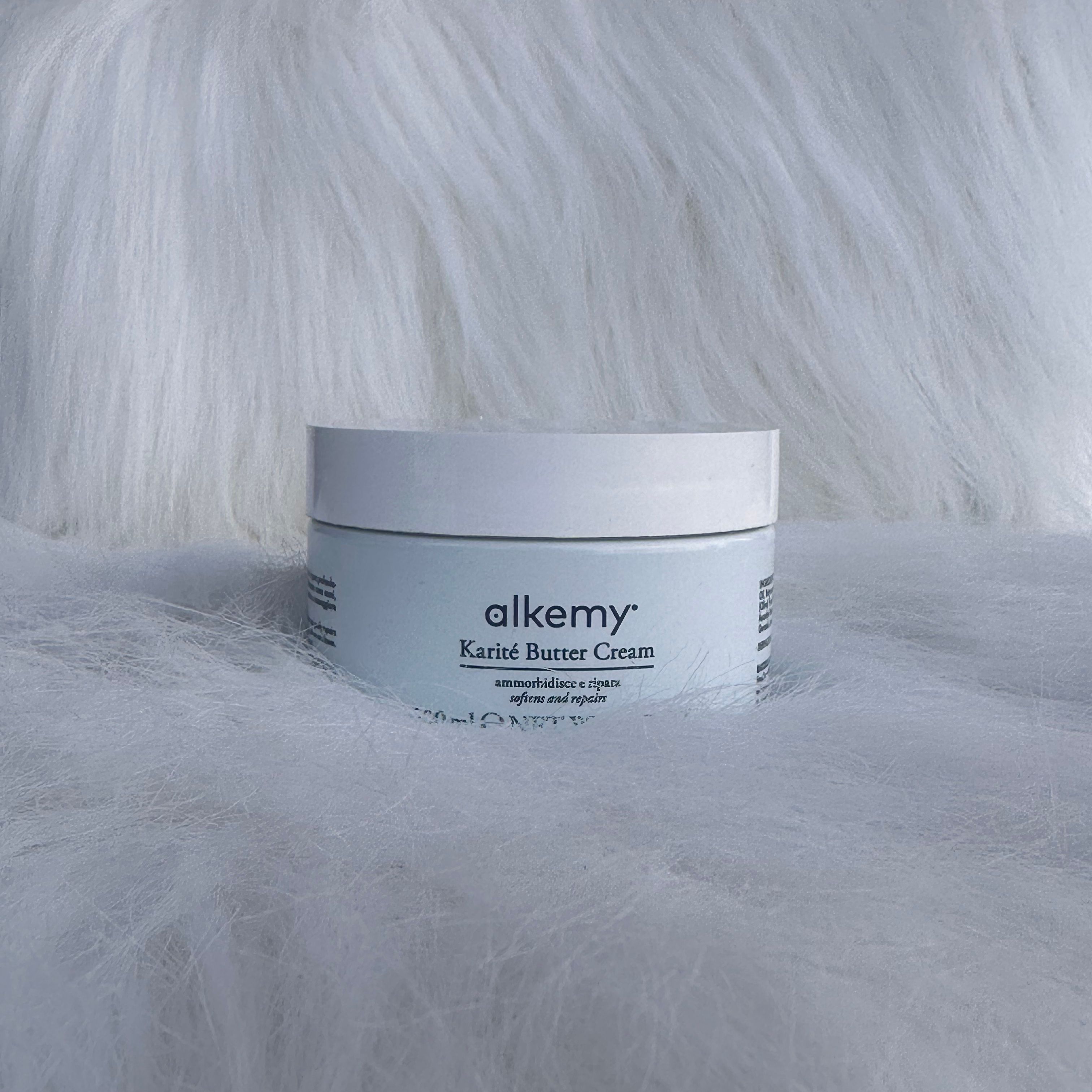 Een witte container met het etiket 'alkemy Karité Butter Cream' op een pluizige ondergrond.
