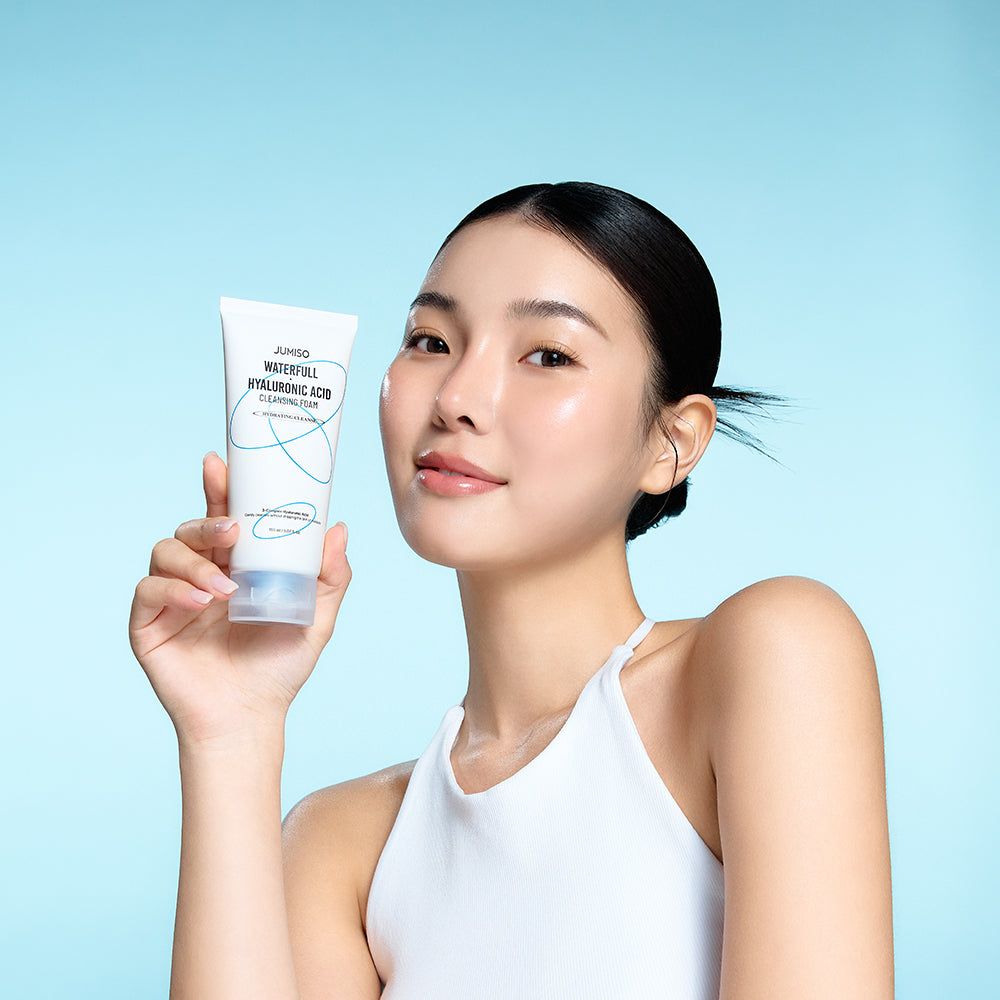 Une femme tient un tube de nettoyant moussant. Sur le tube : JUMISO Waterfull Hyaluronic Acid Cleansing Foam.
