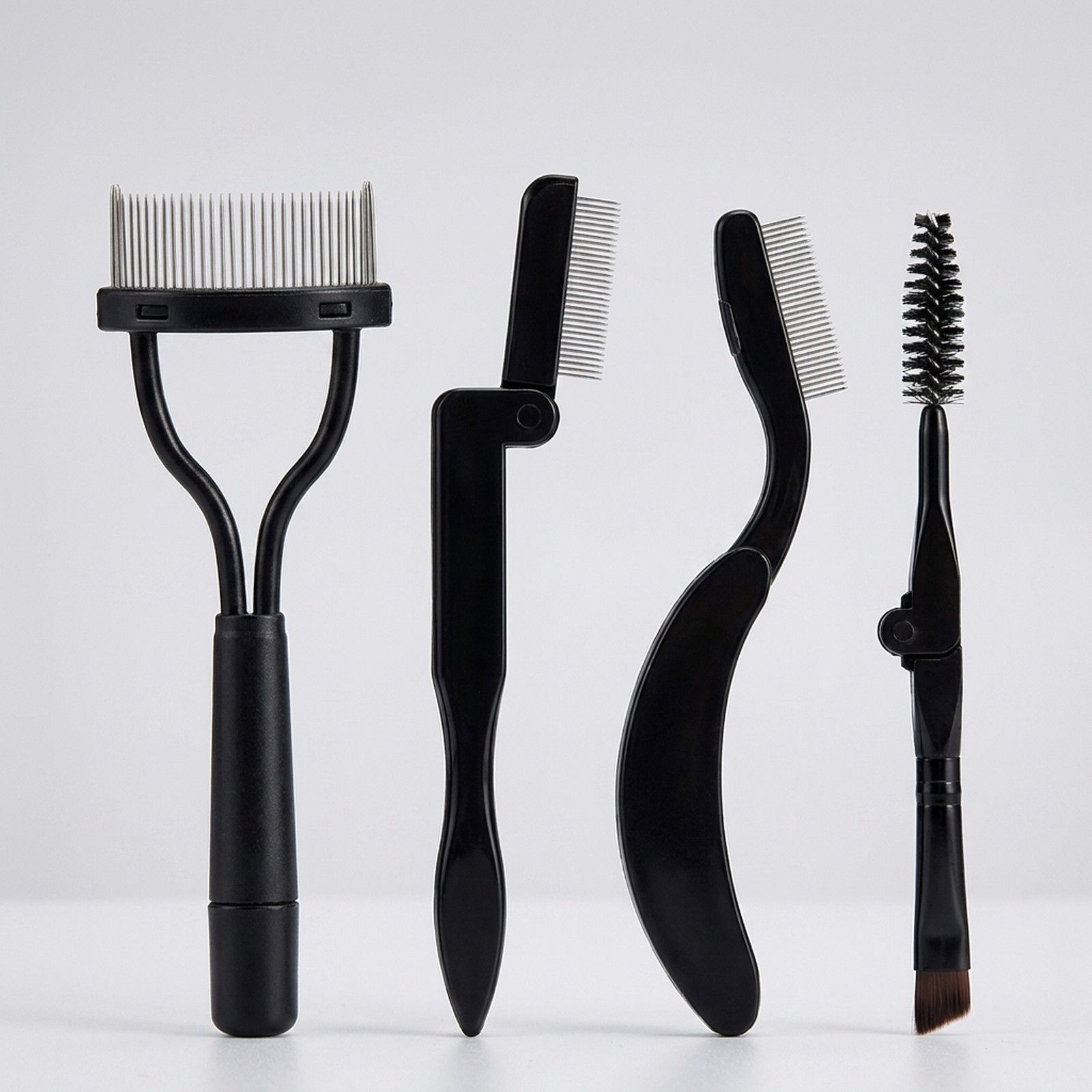 Quatre outils noirs pour cils et sourcils : peigne, peigne pliable, peigne courbé et brosse.