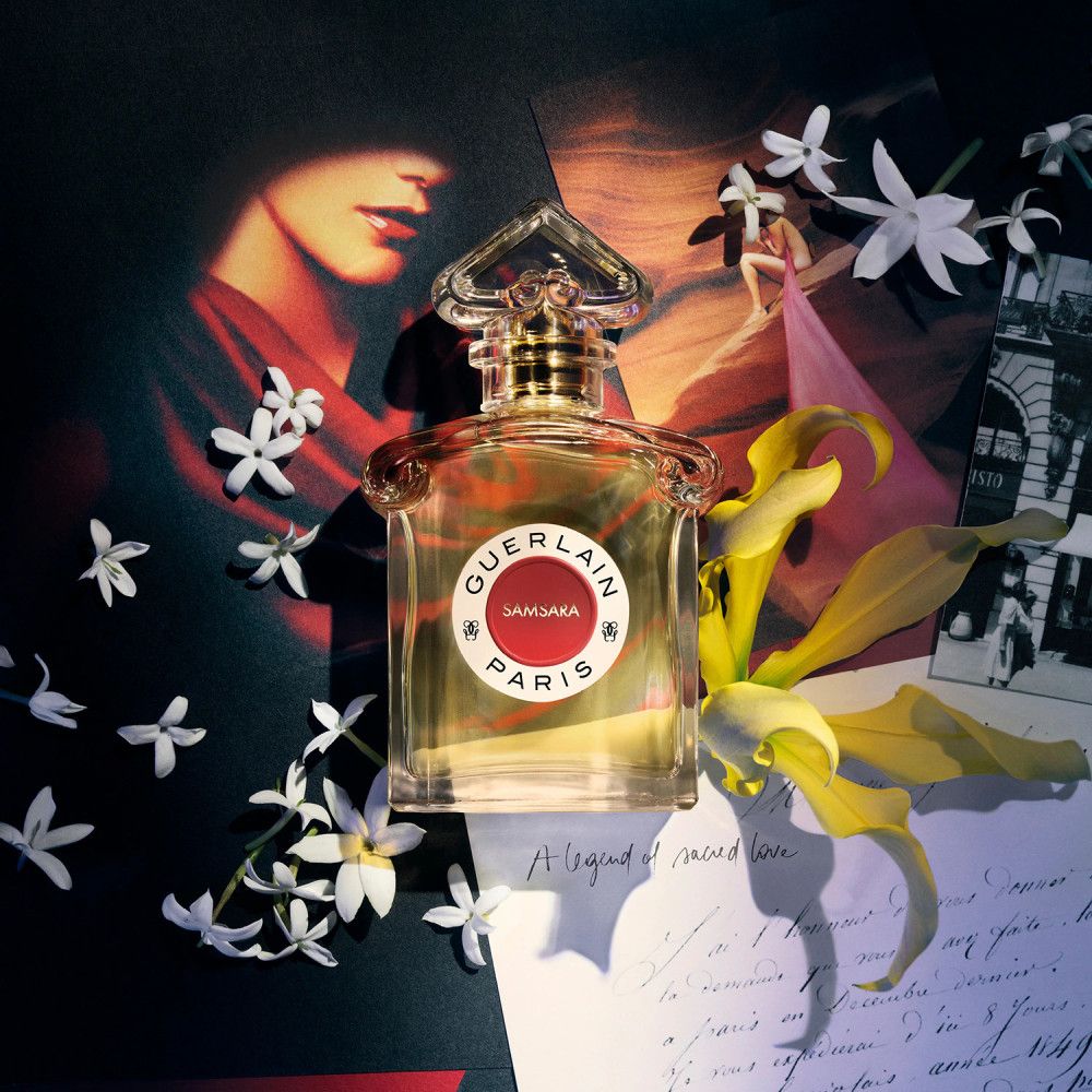 Flacon de parfum Samsara Paris, entouré de fleurs et d'éléments décoratifs. Étiquette rouge avec inscription.