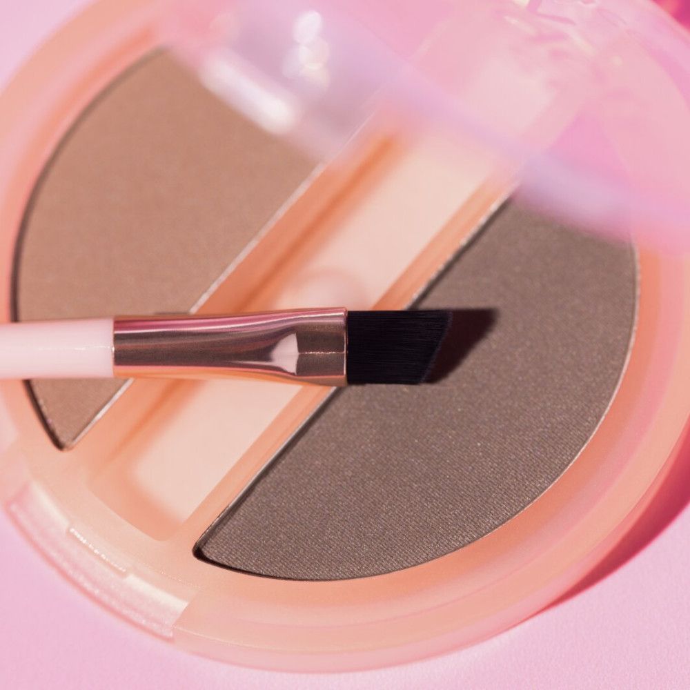 Gros plan d'un ensemble Essence Brow Powder Duo avec pinceau. Deux couleurs de poudre à sourcils sont visibles.
