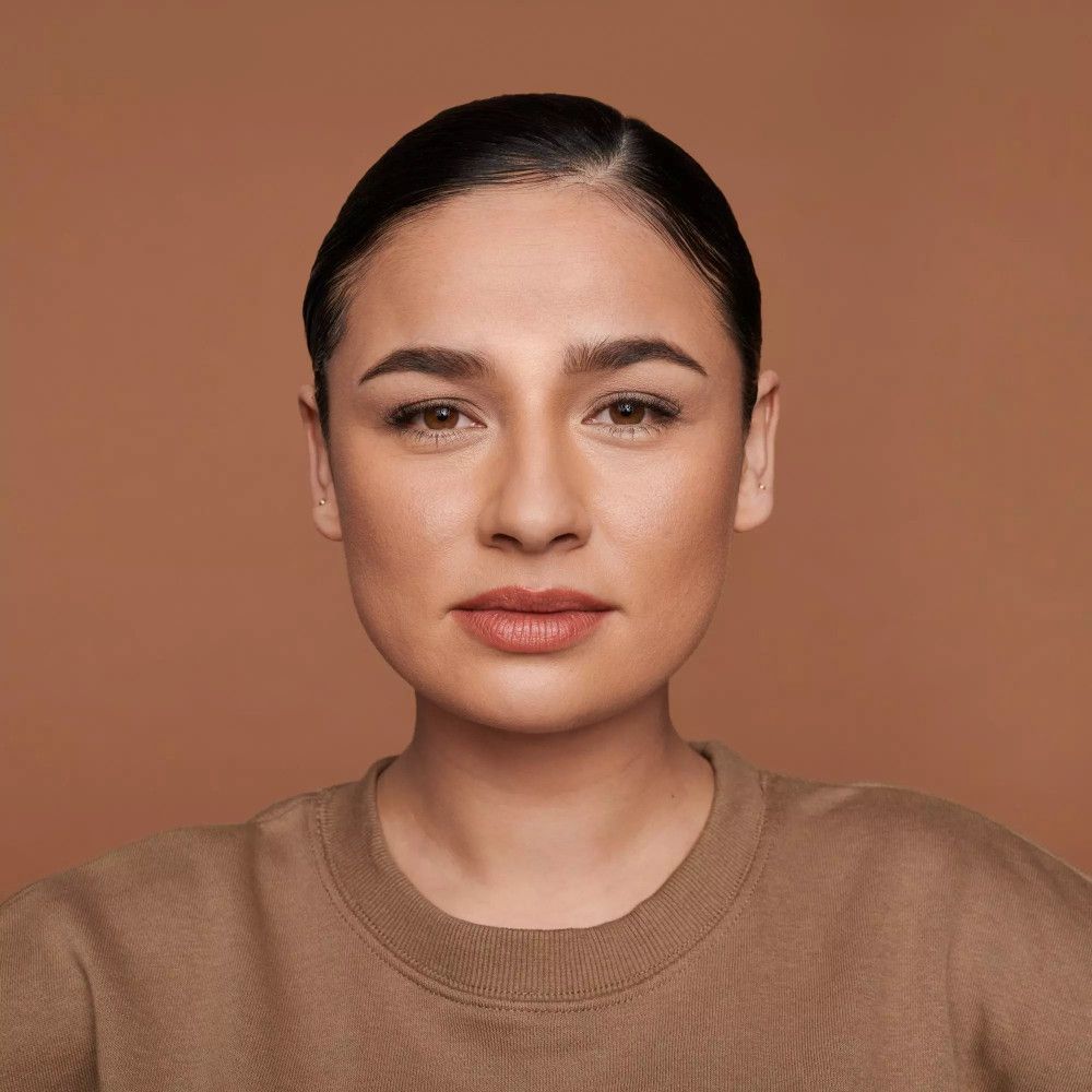 Portrait d'une femme à la peau lisse. Elle porte un pull brun. Maquillage naturel.