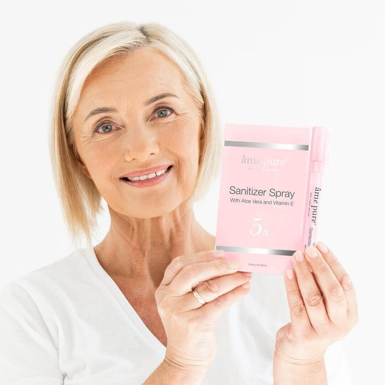 Een vrouw die een roze doos met âme pure Sanitizer Spray en een los flesje vasthoudt.
