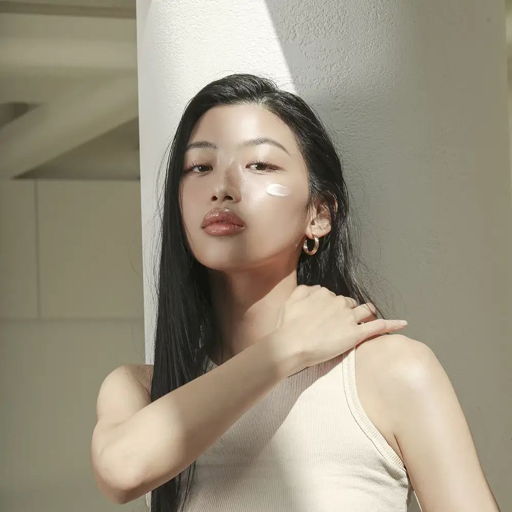 Vrouw met lang, donker haar en oorbellen. Crème op de huid. Natuurlijk licht.