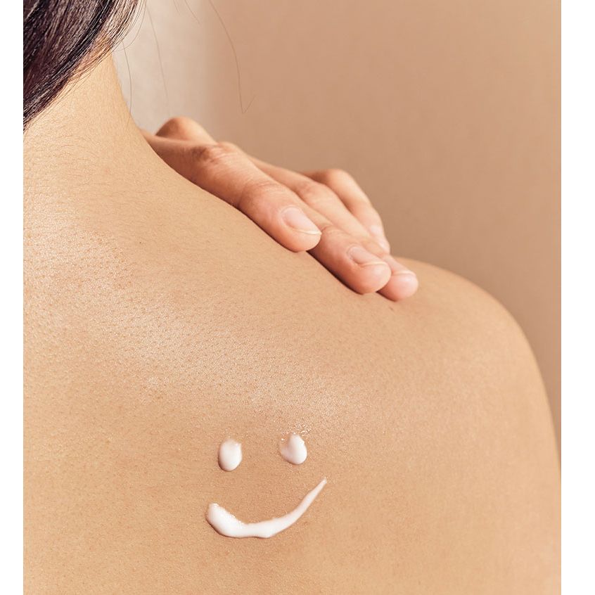 Close-up van een persoon die crème op de rug aanbrengt. Crème in de vorm van een lachend gezicht.