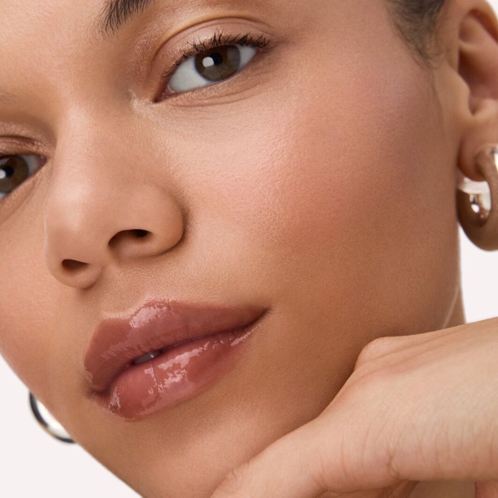 Close-up van een gezicht met glanzende lipgloss op de lippen. De persoon ondersteunt de kin met de hand.