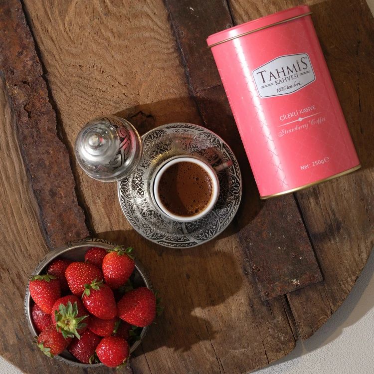 Koffie in kopje, aardbeien in schaal, blik 'Tahmis Kahvesi'. Op houten ondergrond.
