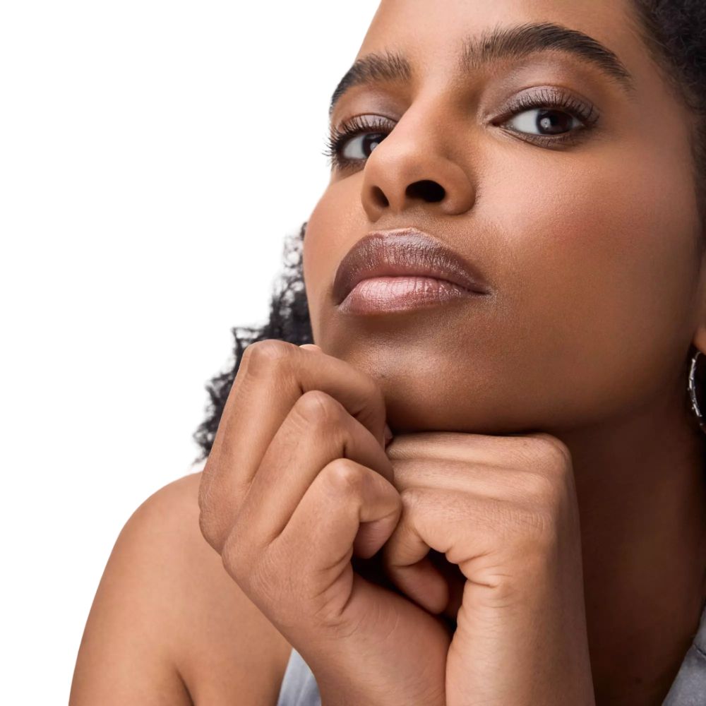 Close-up van een vrouw met opgemaakte lippen. De lippen glanzen. Handen onder de kin.