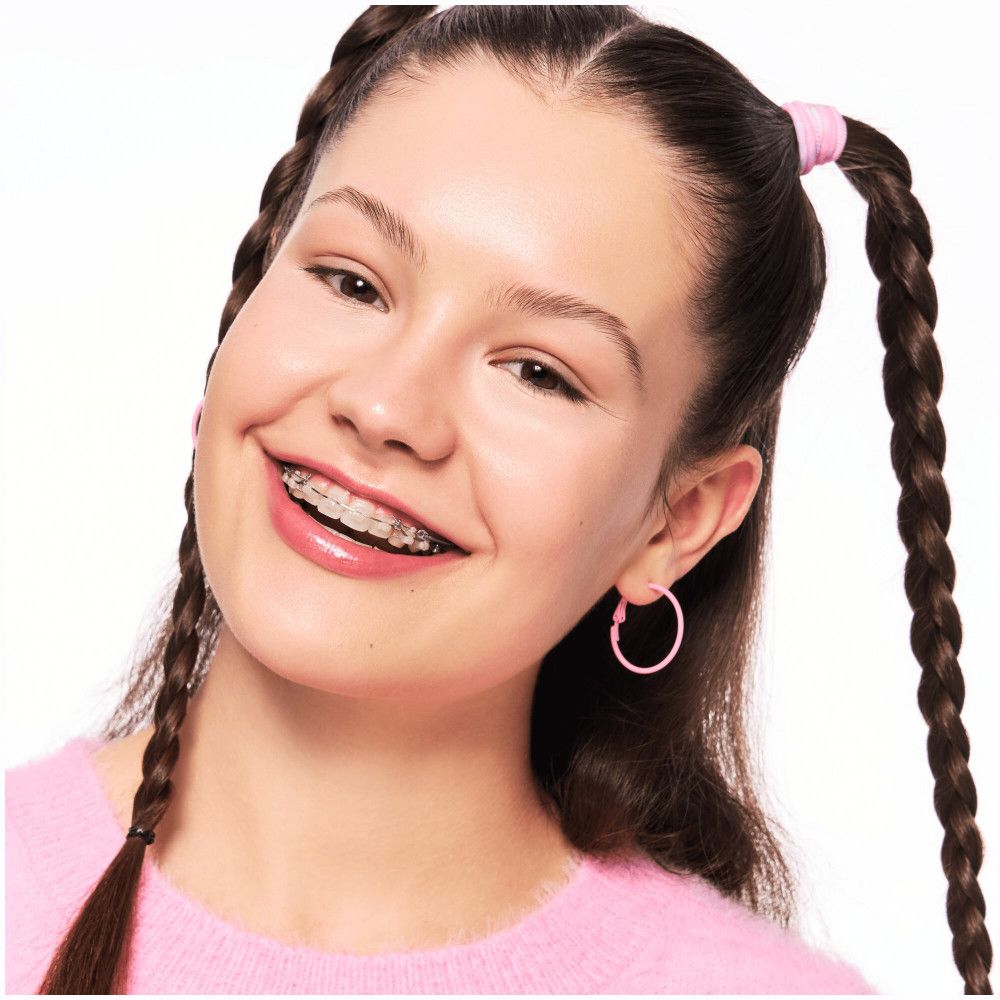 Portrait d'une jeune fille avec des tresses, des boucles d'oreilles roses et un appareil dentaire.