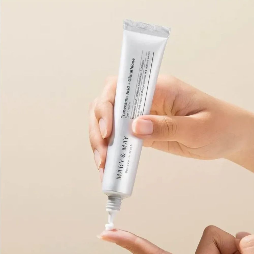 Une main tient un tube de crème contour des yeux Mary & May, une petite quantité est appliquée sur un doigt.