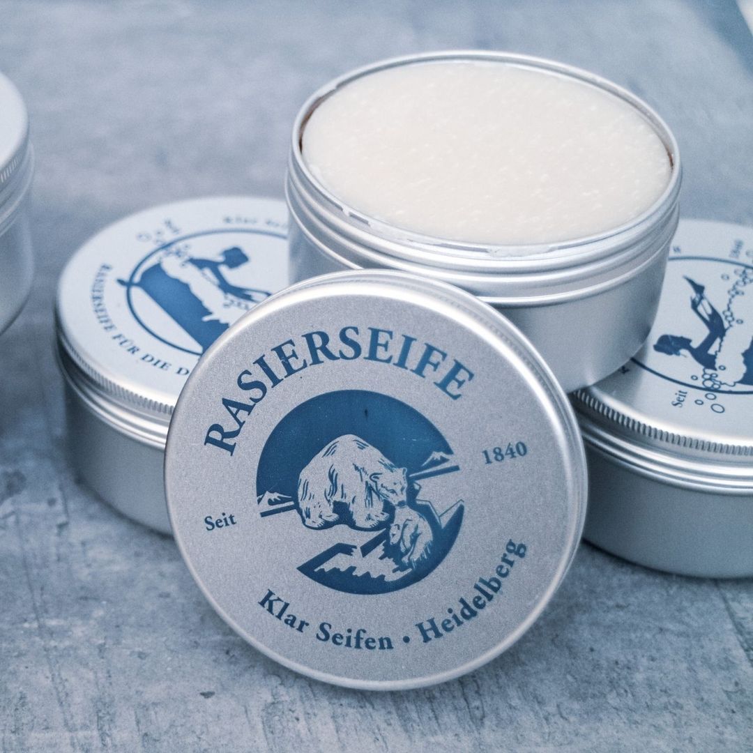 Meerdere scheerzeepblikken, één geopend. Op deksels logo en tekst: Rasierseife, Klar Seifen, Heidelberg. Metalen blikken.