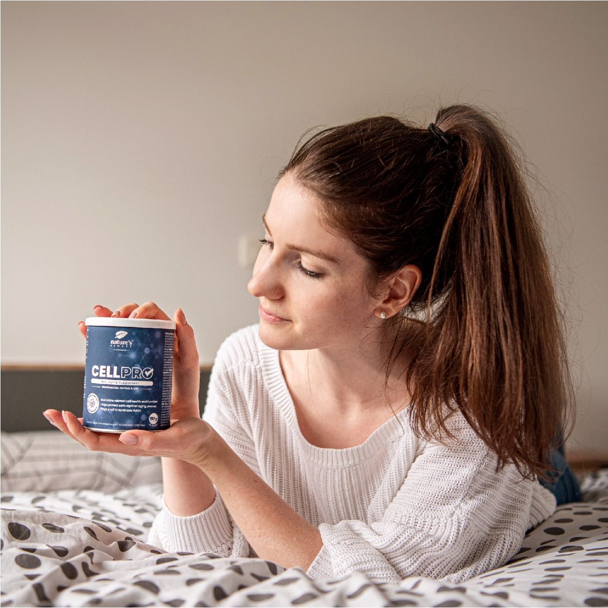Femme tenant boîte Nature's Finest Cell PRO. Inscription: CELL PRO, Anti Aging Supplement, Nicotinamide, Haritaki & Q10.