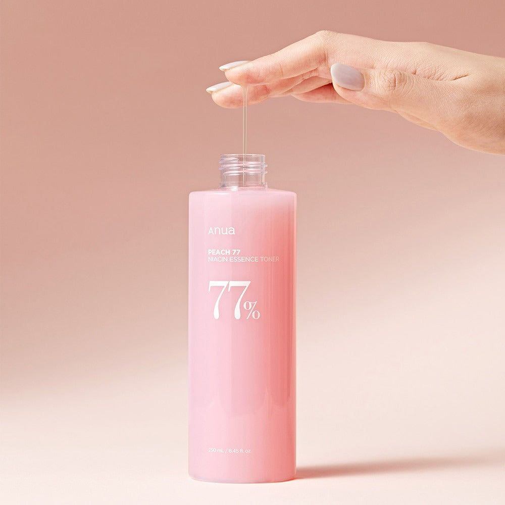 Roze fles met witte dop. Hand houdt vloeistof vast. Opschrift: Peach 77 Niacin Essence Toner. 77% in witte letters.