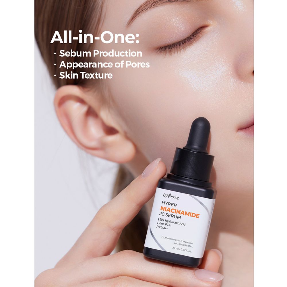 Flacon de sérum avec compte-gouttes dans une main. Inscription : ISNTREE Hyper Niacinamide 20 Serum. Visage en arrière-plan. Flacon noir.