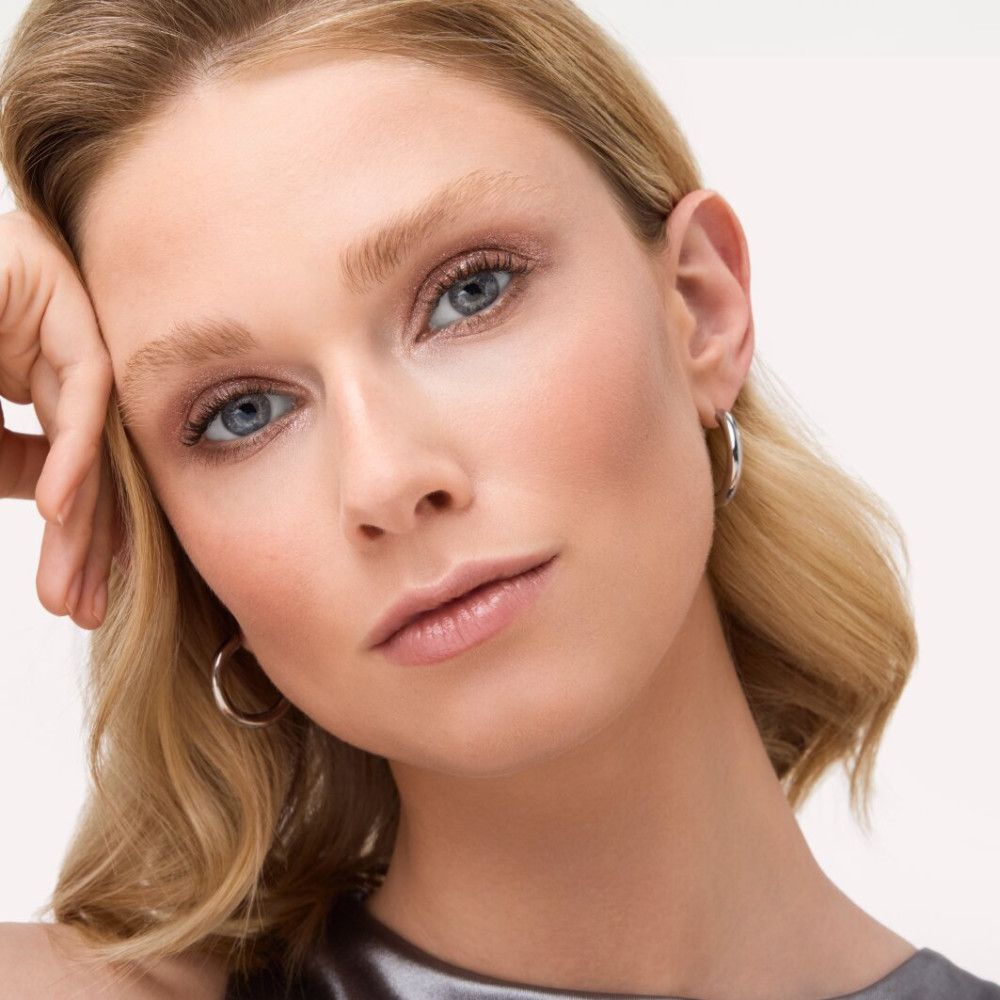 Portret van een vrouw met blond haar en blauwe make-up. Ze steunt haar hoofd op haar hand.