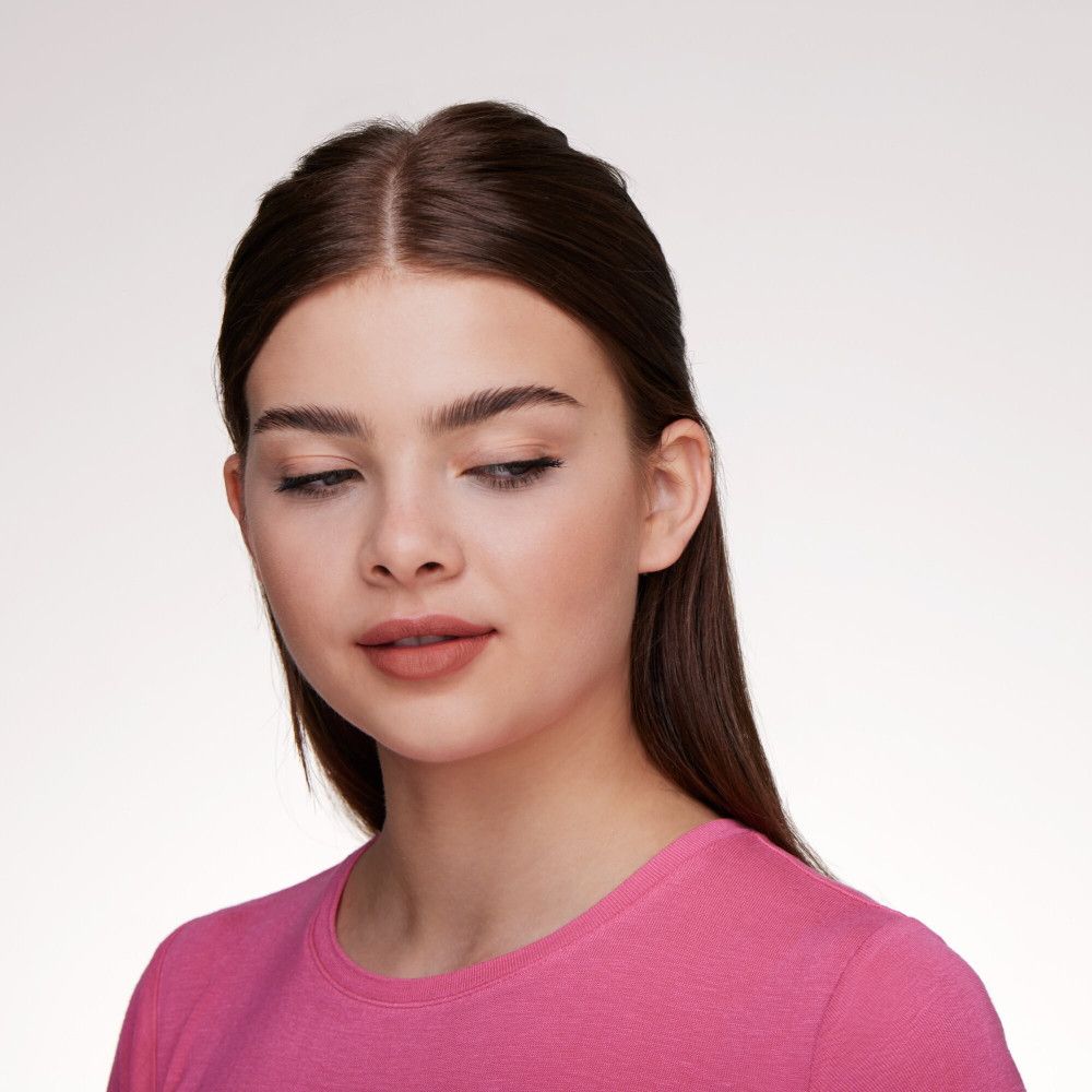 Gros plan d'une femme en haut rose. Elle regarde vers le bas, les lèvres légèrement entrouvertes.