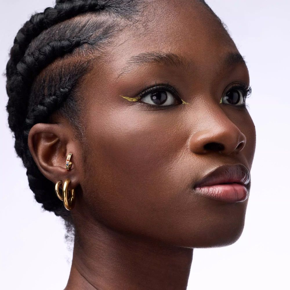 Gros plan d'une femme avec des tresses. Elle porte un eye-liner doré. Elle porte des boucles d'oreilles dorées.