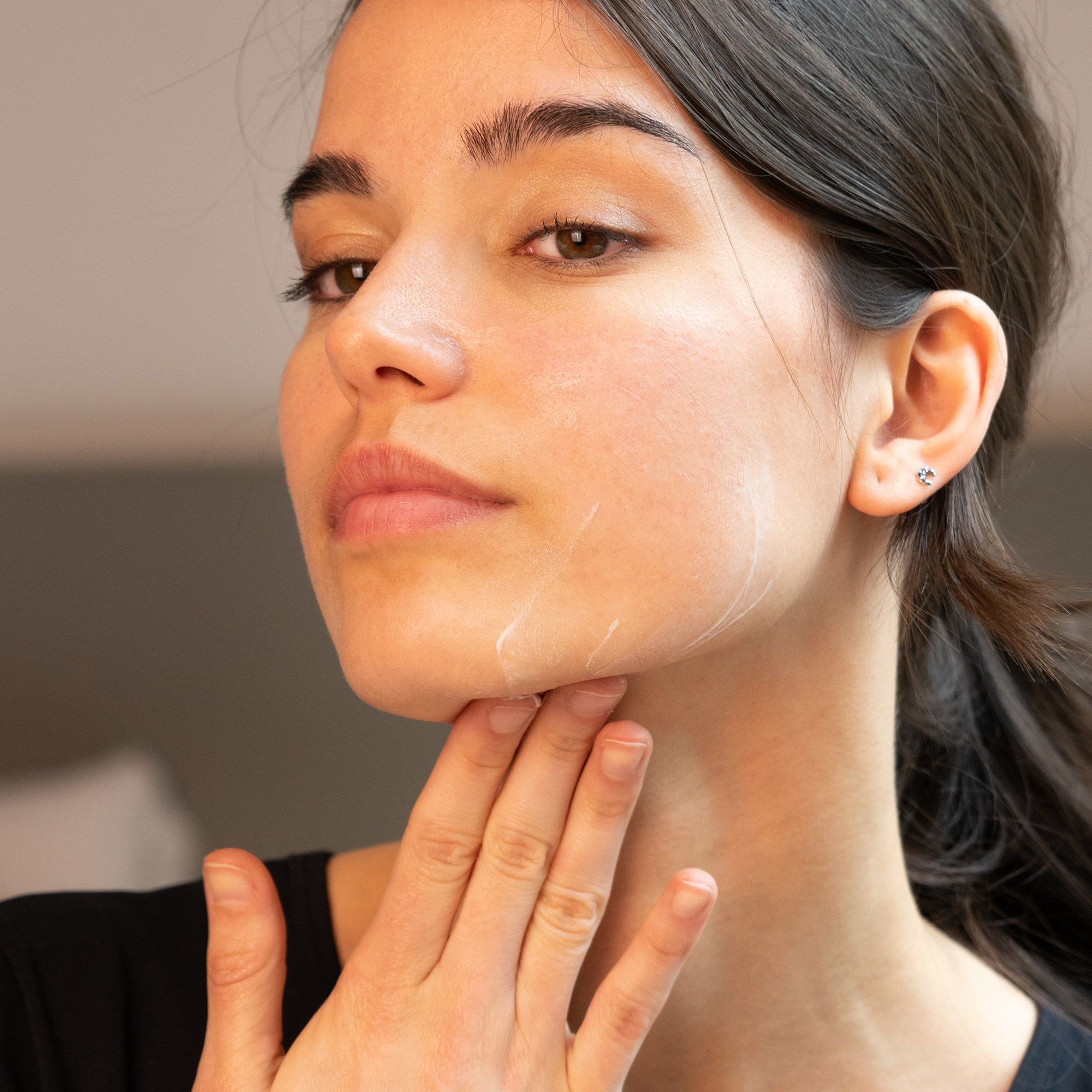 Femme se touchant le visage. Application de crème. Aucune désignation de produit visible.