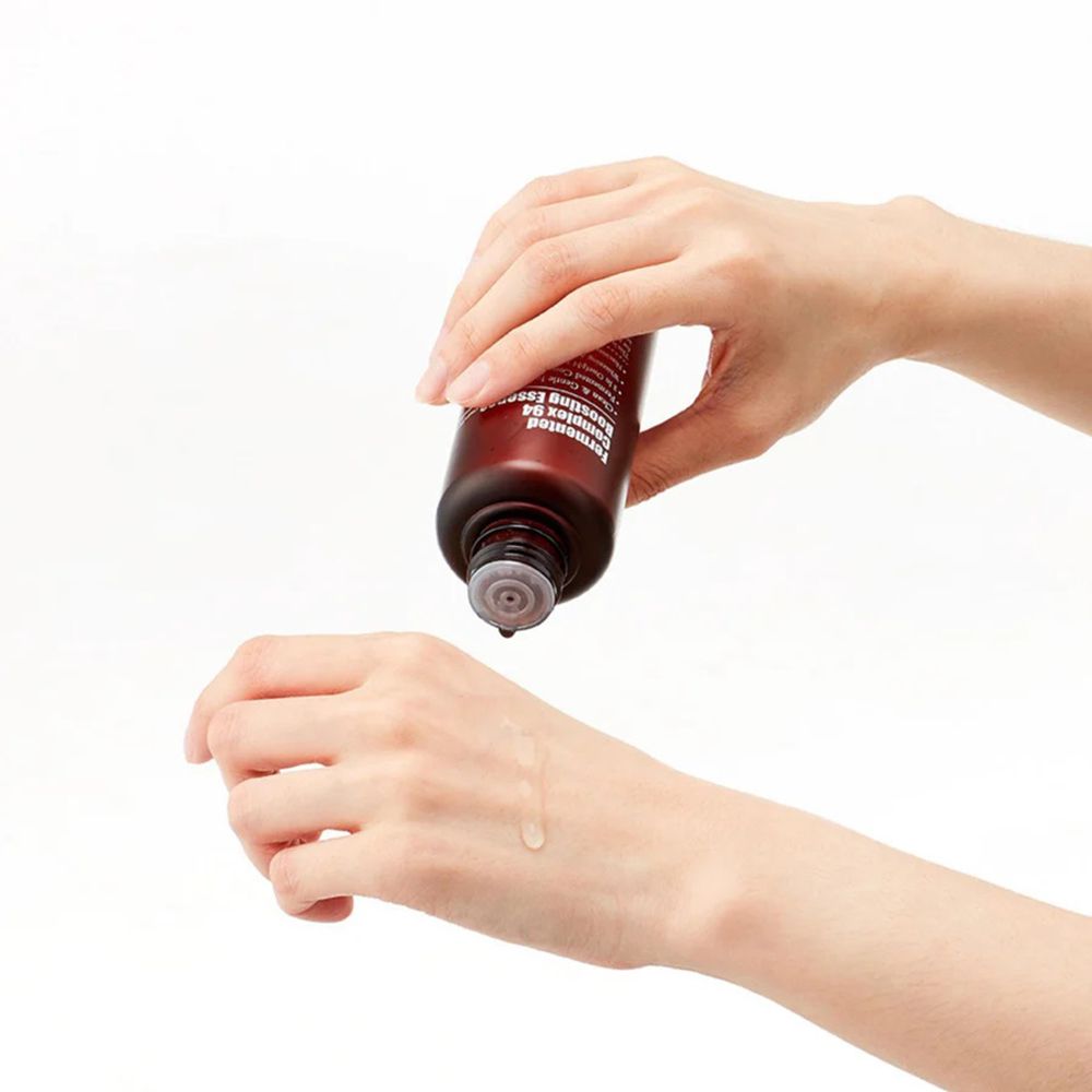 Mains tenant un flacon marron. Liquide coulant sur la paume. Produit: Fermented Complex 94 Boosting Essence.