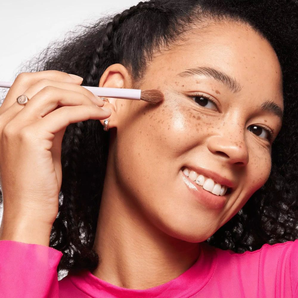 Vrouw met blending brush. Roze handvat, bruine borstelharen. Ze brengt het product aan op haar huid.