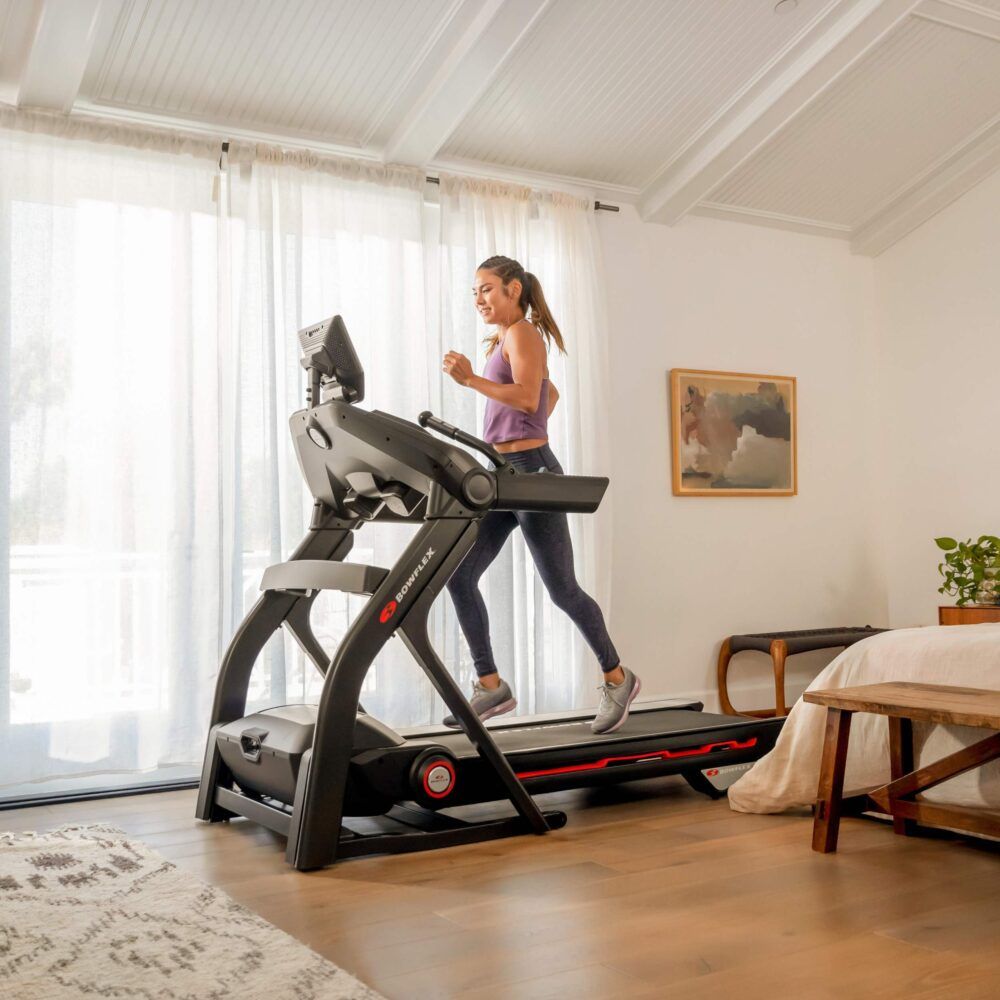 Femme courant sur un tapis roulant T25. Design noir. Console avec écran. Logo Bowflex.