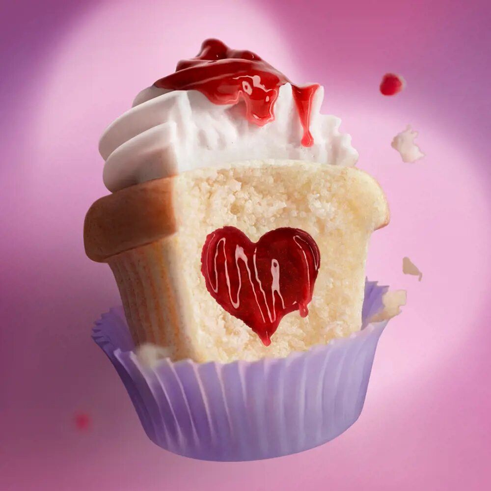 Cupcake met hartvormige vulling en slagroom. Rode siroop druipt. Paarse papieren vorm.