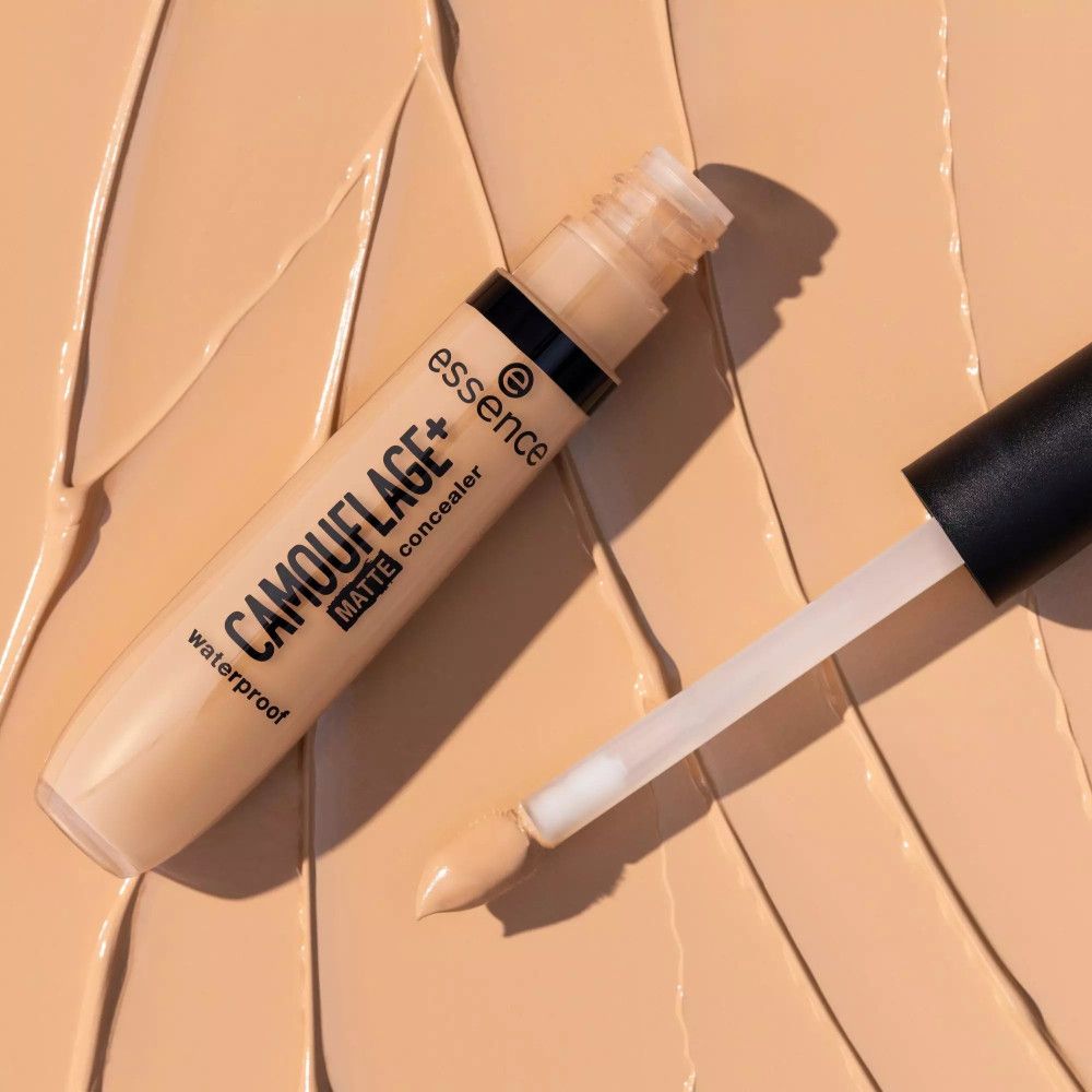 Tube de correcteur et applicateur sur fond beige. Inscription: CAMOUFLAGE+ matte concealer, waterproof. Marque: essence.