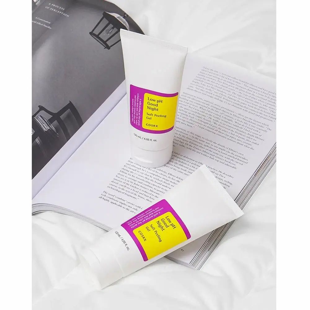 Deux tubes sur un livre ouvert. Inscription : Low pH Good Night Soft Peeling Gel. Marque COSRX. Fond blanc.