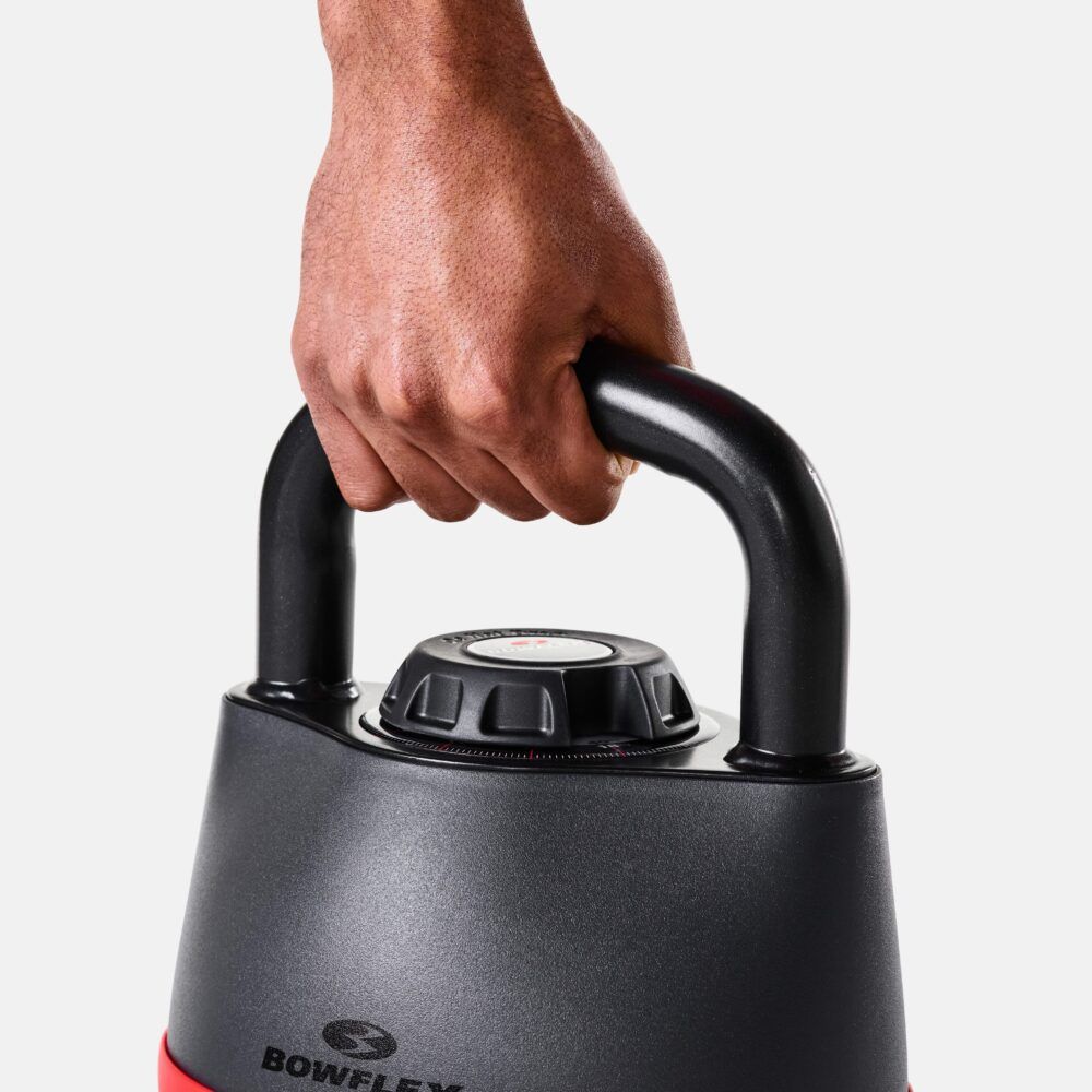 Hand die kettlebell vasthoudt. Zwarte kettlebell met rode band. Bowflex-logo zichtbaar.