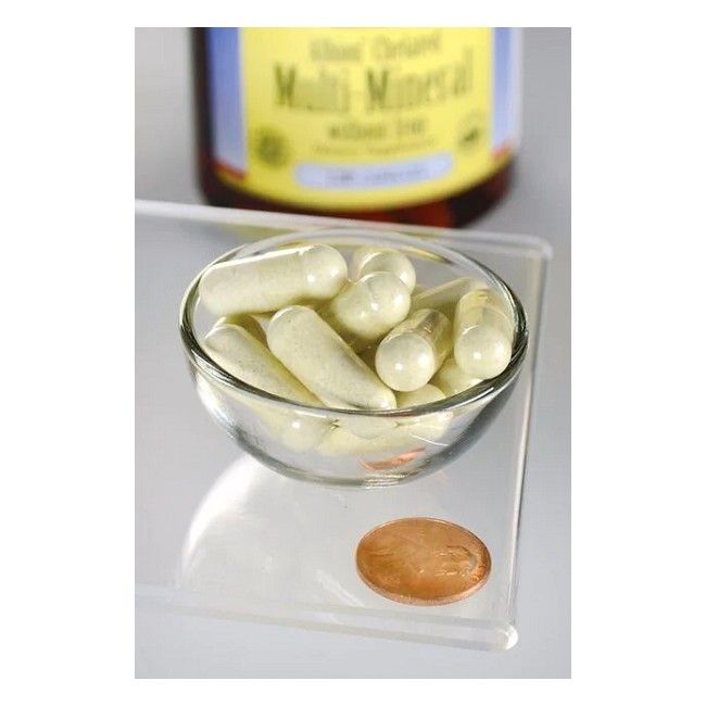 Gélules dans un bol en verre. En arrière-plan, flacon SWANSON Multi-Mineral sans fer Albion. Une pièce de monnaie à côté.