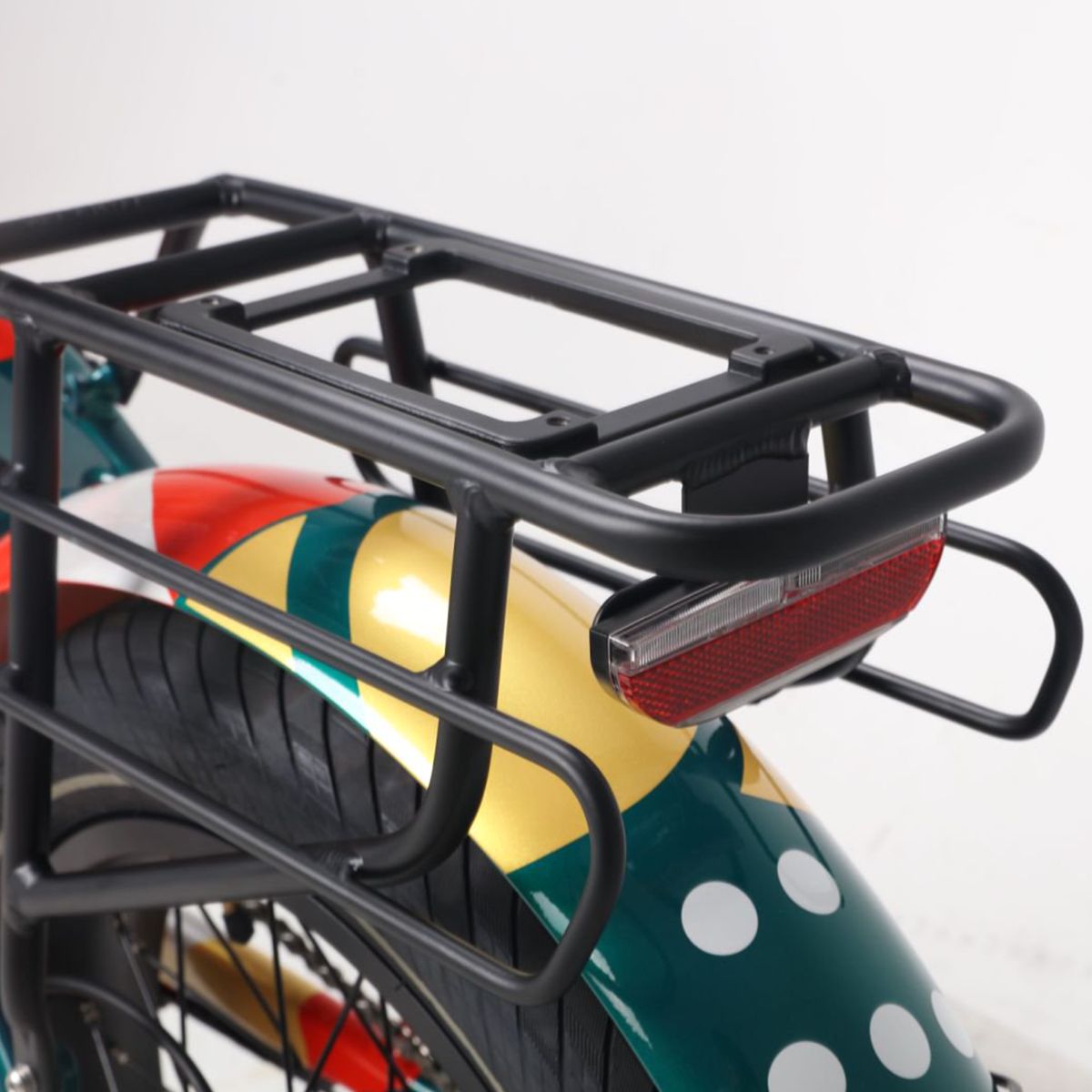 Porte-bagages et feu arrière d'un vélo électrique. Porte-bagages noir, feu arrière rouge. Design vert-jaune du garde-boue avec points blancs.