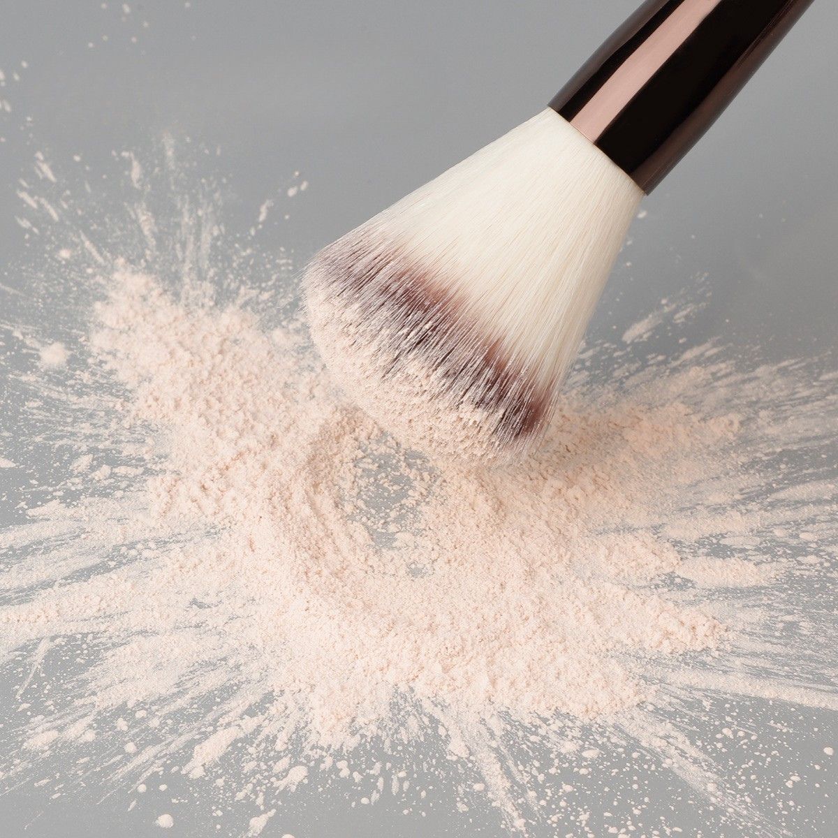 Un pinceau de maquillage aux poils blancs et au manche sombre, trempé dans une poudre rose pâle.