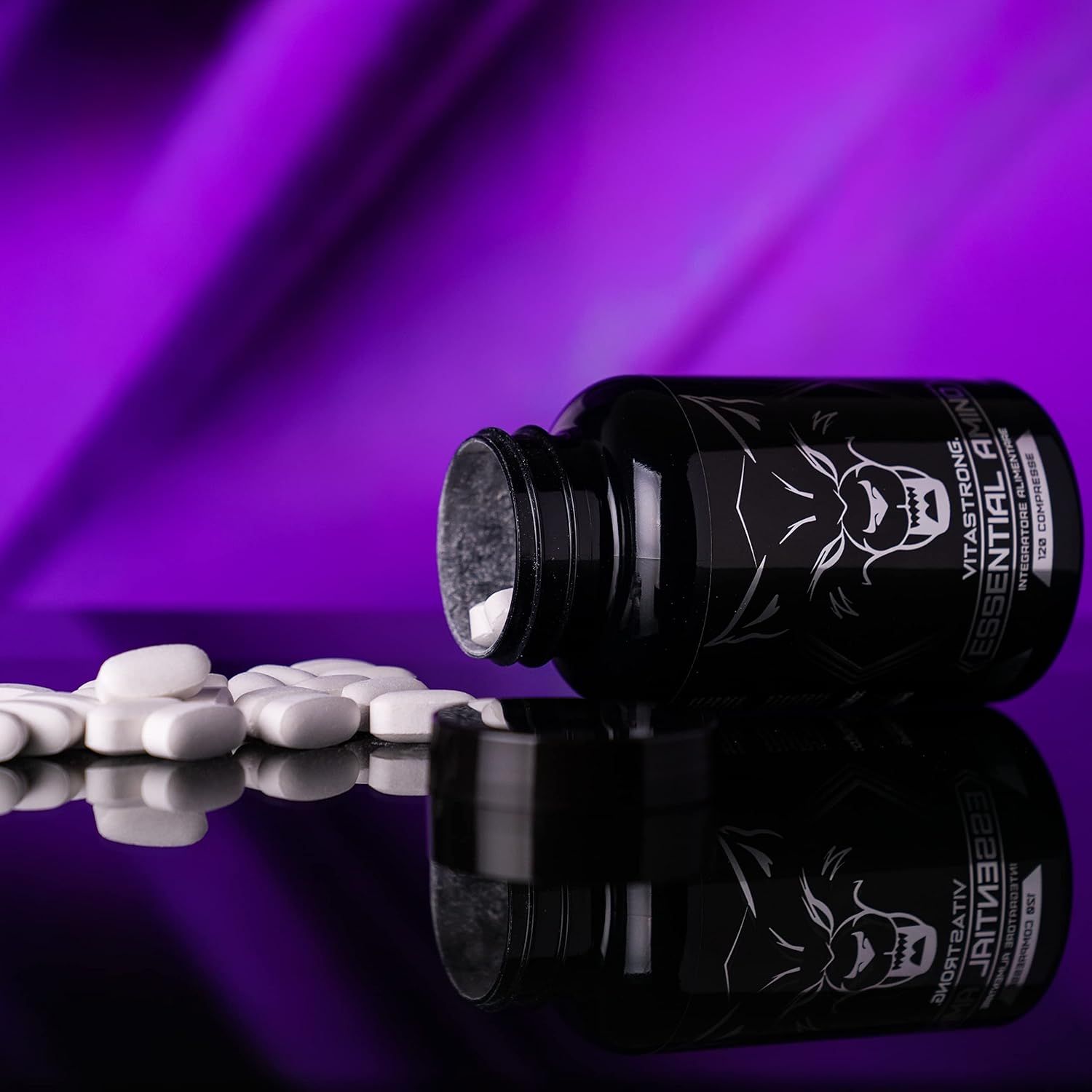 Zwarte fles Vitastrong Essential Amino, tabletten ernaast. Opschrift en wolf logo. Paarse achtergrond.