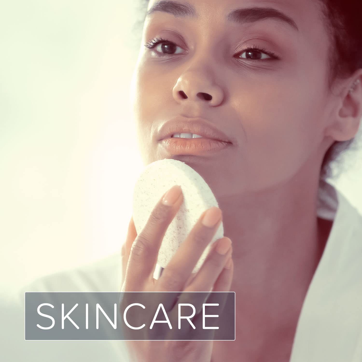 Vrouw in witte badjas, reinigt haar gezicht met een spons. Tekst: SKINCARE.