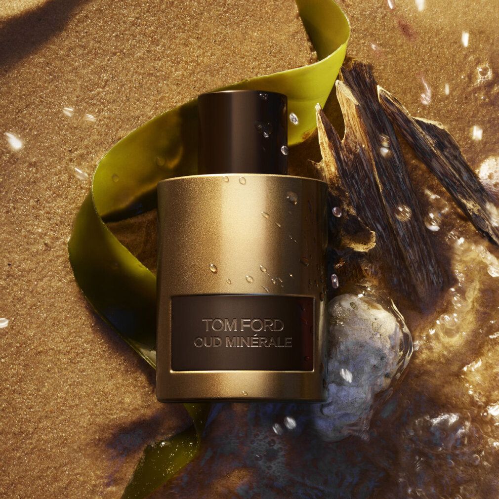Gouden fles, bruine dop, rechthoekig etiket met tekst TOM FORD OUD MINERALE. Op zand, met water.