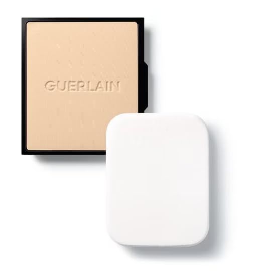 Fond de teint compact et éponge. Fond de teint compact noir avec inscription Guerlain. Éponge blanche à côté.