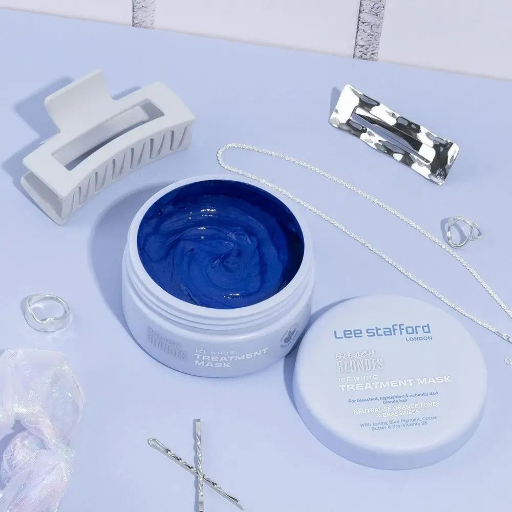 Boîte blanche ouverte avec masque bleu, à côté d'accessoires pour cheveux et de bijoux sur fond clair.