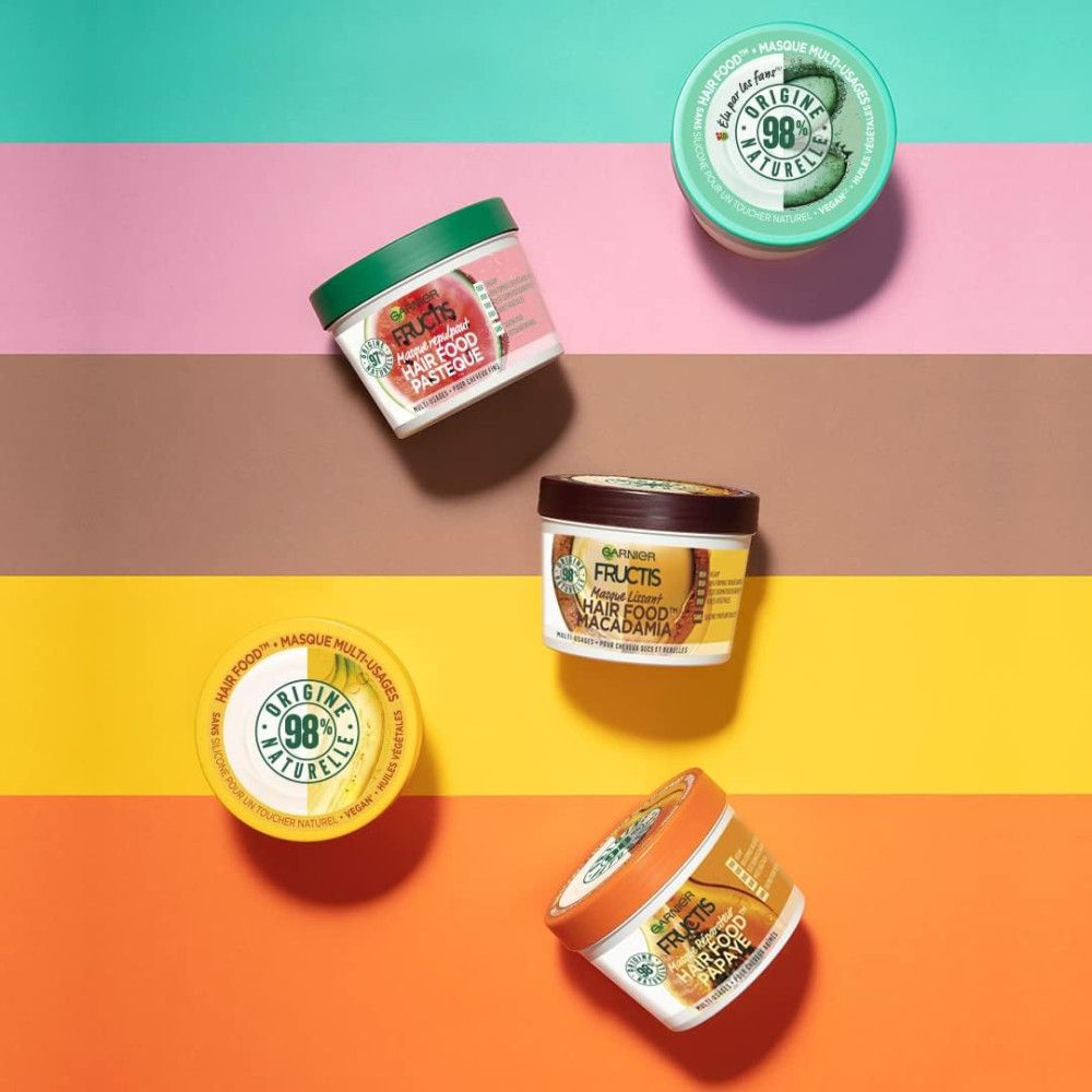 Plusieurs pots Garnier Fructis Hair Food sur fond coloré. Couvercles avec inscriptions. Différentes couleurs.