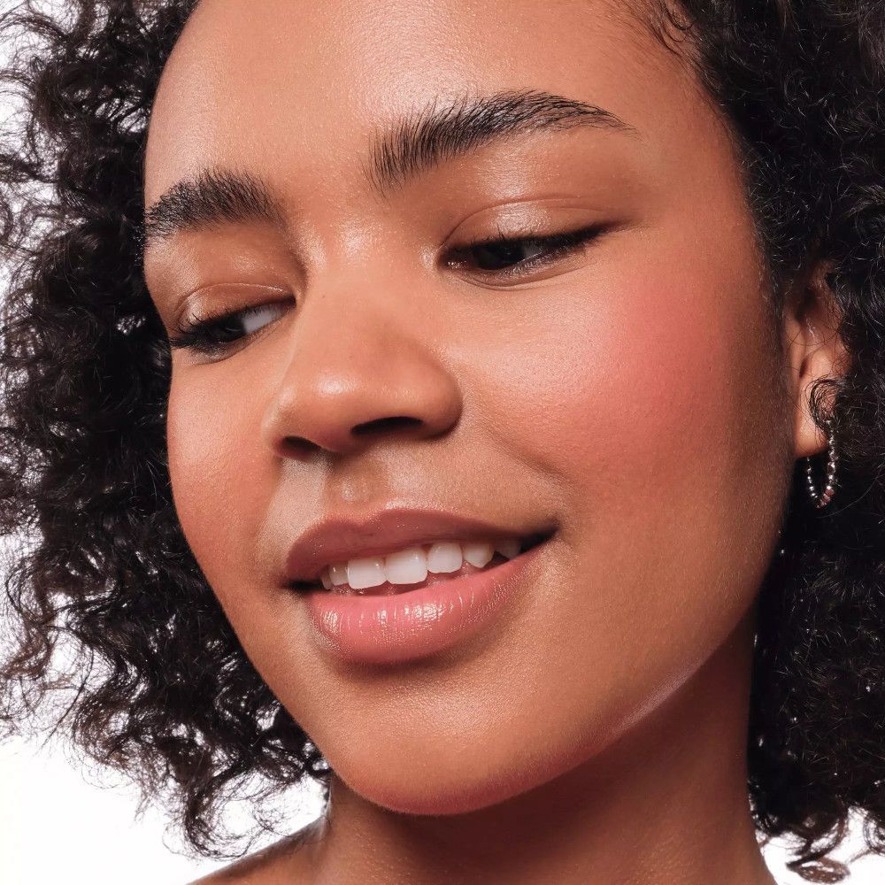 Gros plan d'une femme avec du blush sur les joues. Elle sourit légèrement.