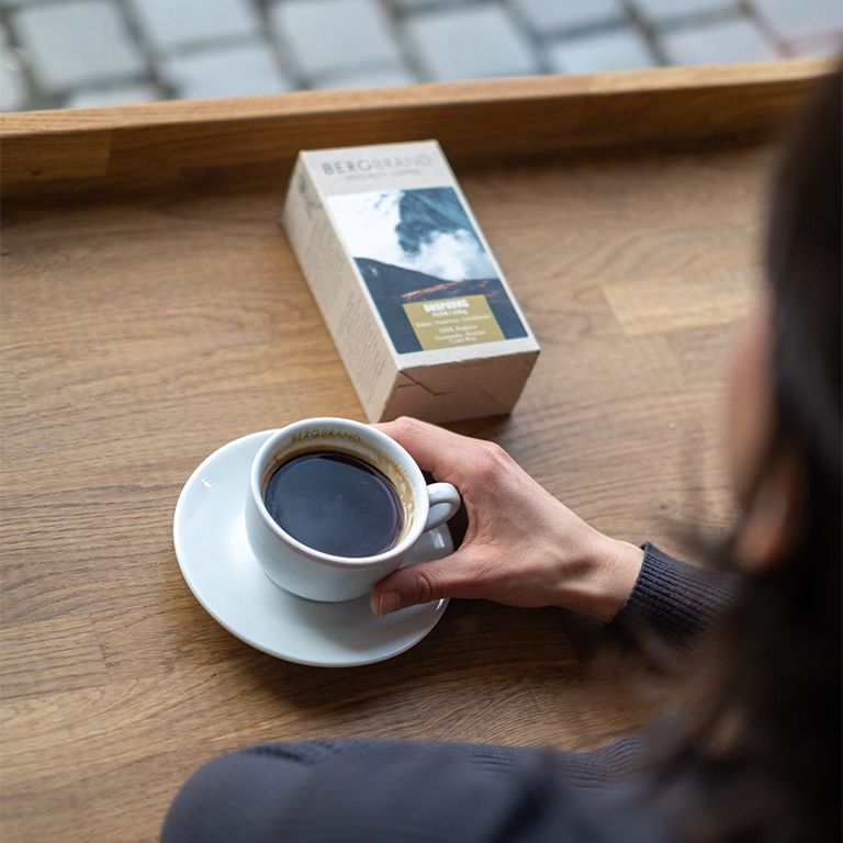 Tasse de café et paquet. Texte: BERGBRAND. Tasse de café avec café. Paquet avec motif montagne. Ursprung, Filter, 250g, 100% Arabica, cacao, noisette, chocolat.