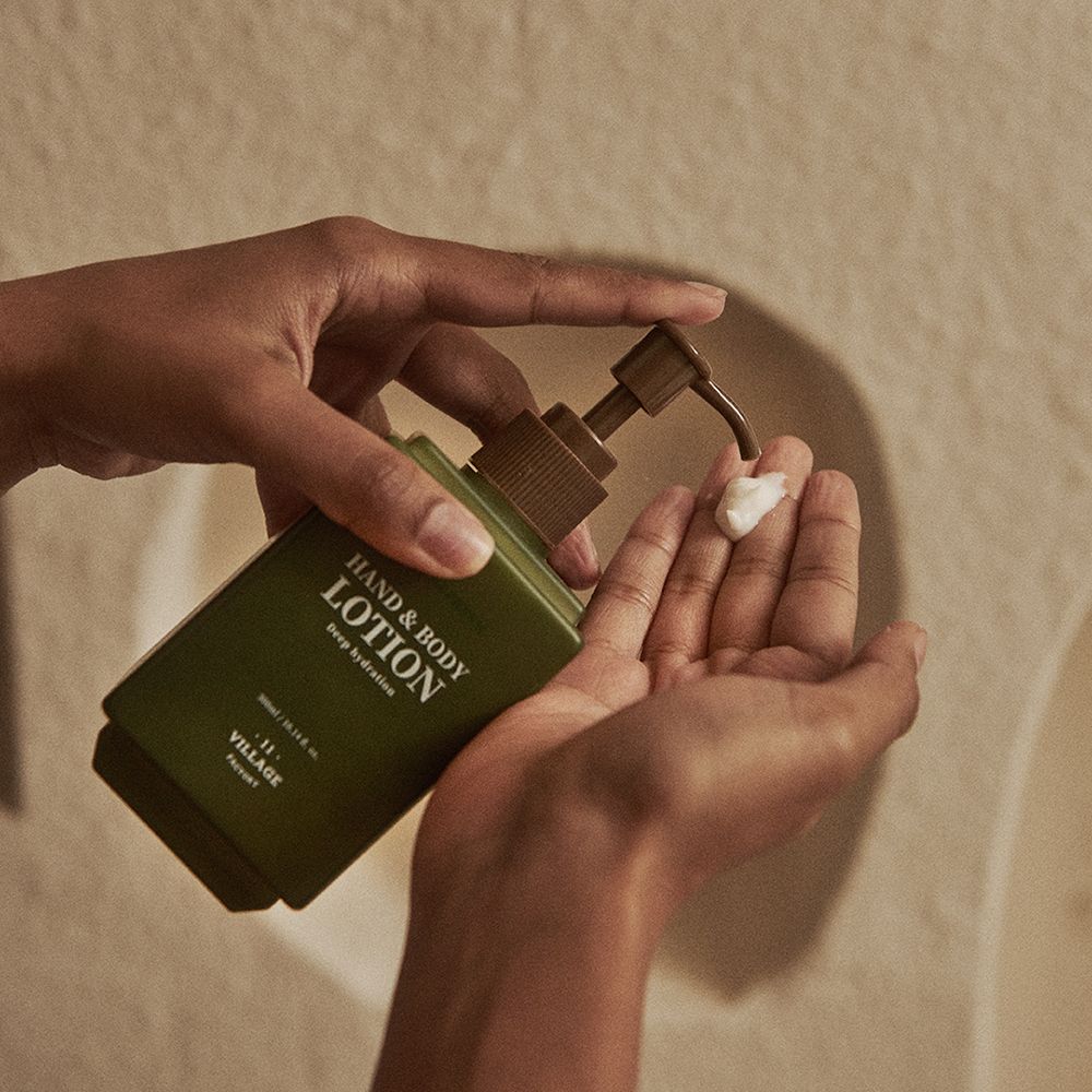 Handen die lotion uit een groene fles met bruine pomp persen. Opschrift: Hand & Body Lotion.