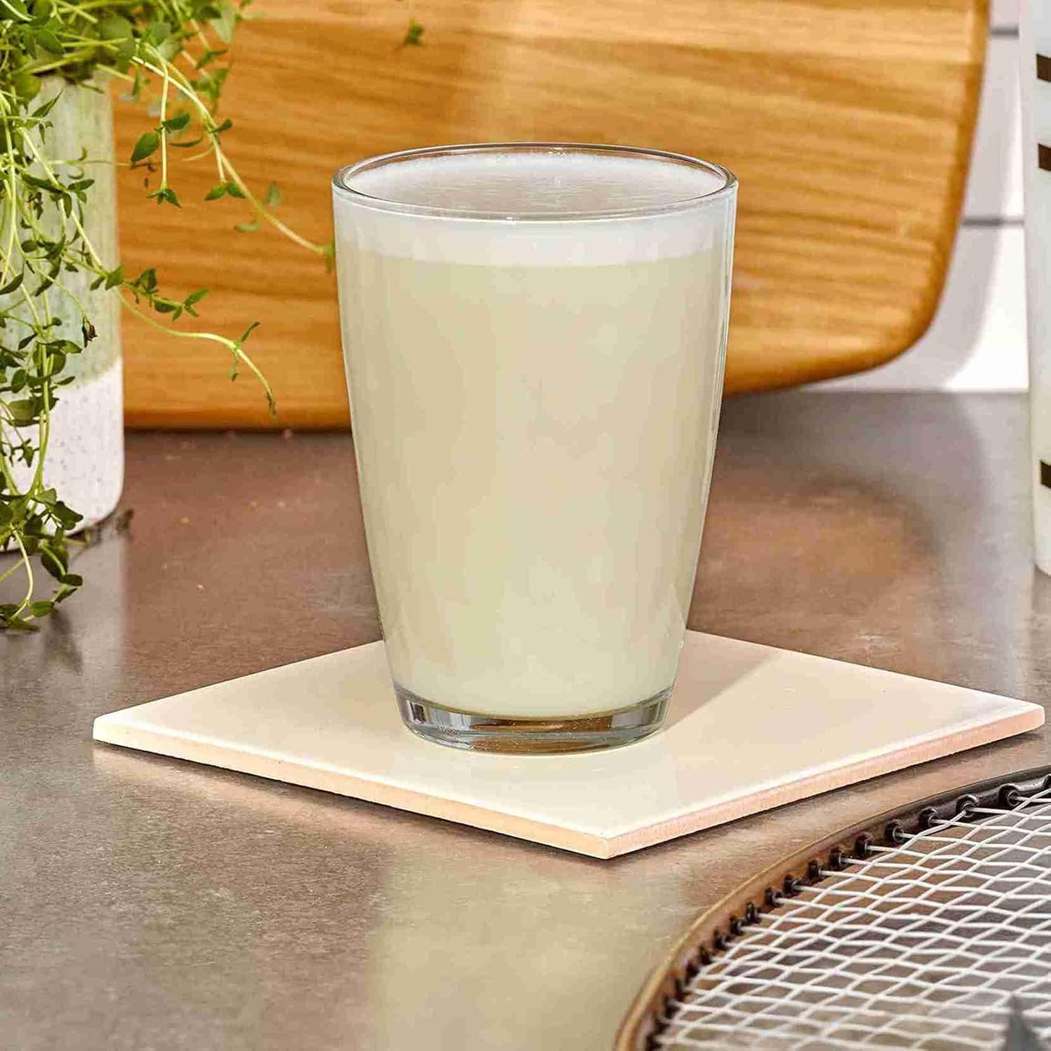 Een glas romige melk staat op een lichte onderzetter op een aanrecht.