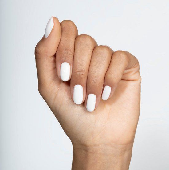 Main avec ongles vernis blancs. Les ongles sont de forme ovale et ont une surface lisse. Le fond est clair.