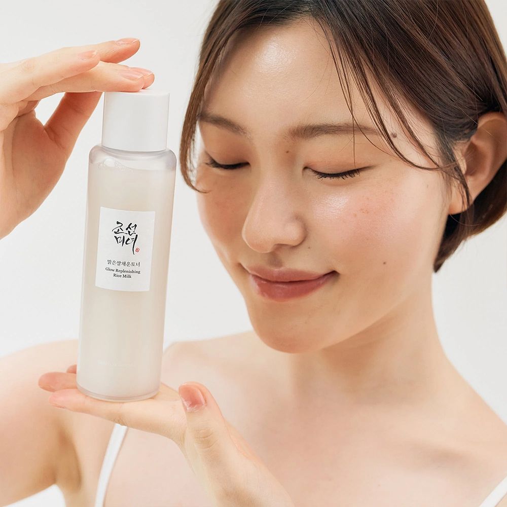 Een vrouw houdt een fles BEAUTY OF JOSEON Glow Replenishing Rice Milk vast.