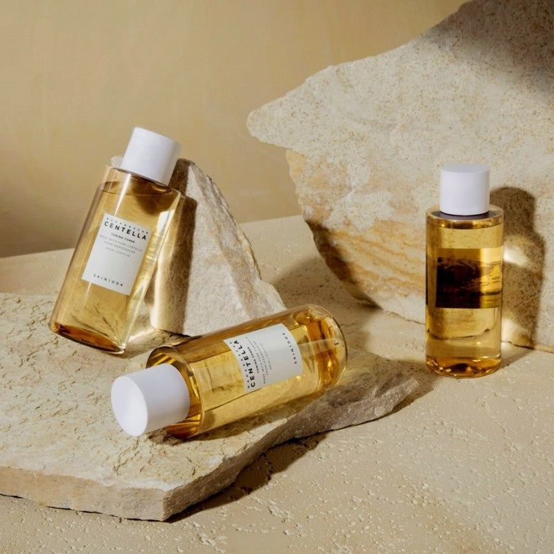 Drie flessen toner op rotsen. Twee flessen liggen, één staat.