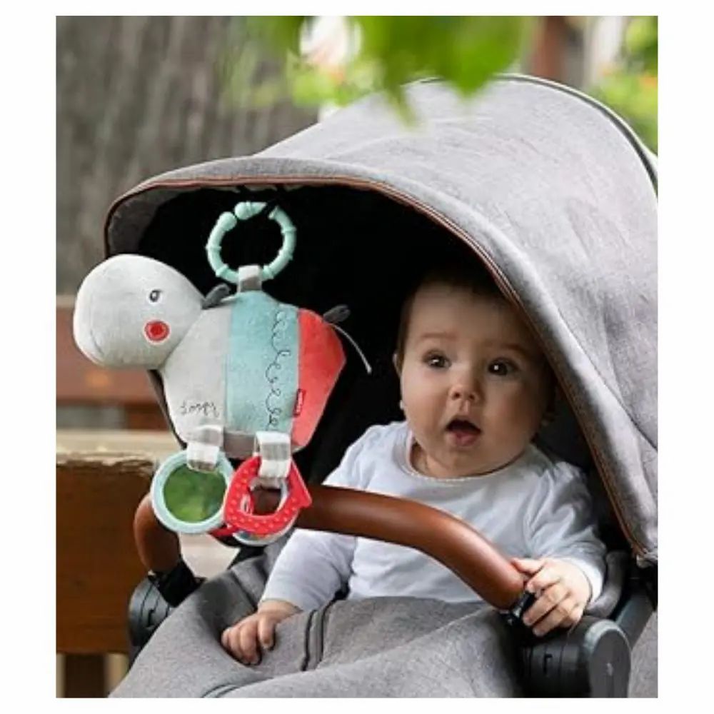 Bébé dans une poussette avec une peluche hippopotame. Le jouet est attaché à la poussette. Bébé regarde.