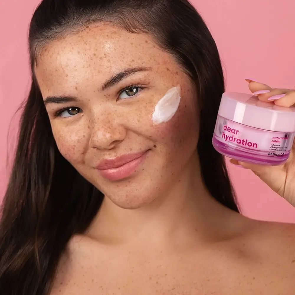 Vrouw met crème op wang, houdt potje vast. Op potje staat "dear hydration" en "BANILA CO".