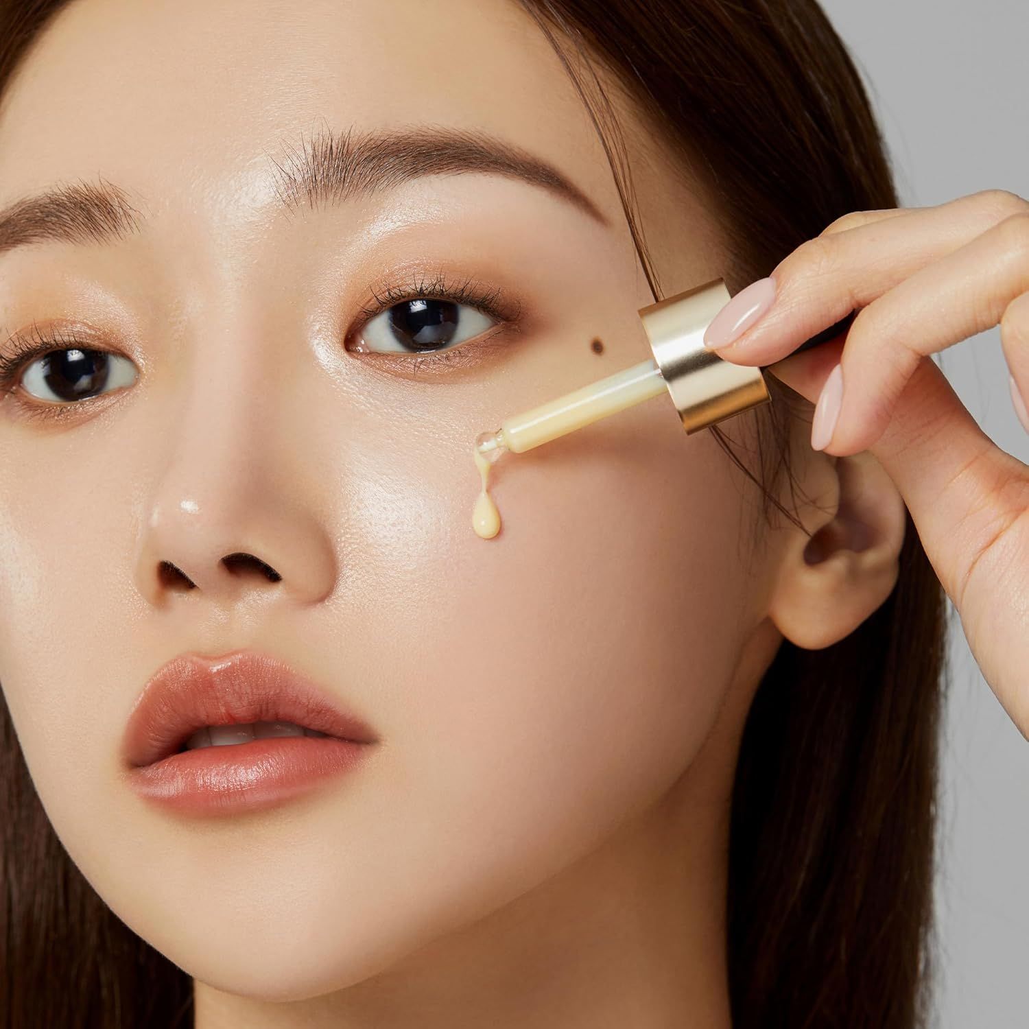 Close-up van een vrouw die serum met een pipet op haar gezicht aanbrengt. Huid glanst. Gouden pipet.