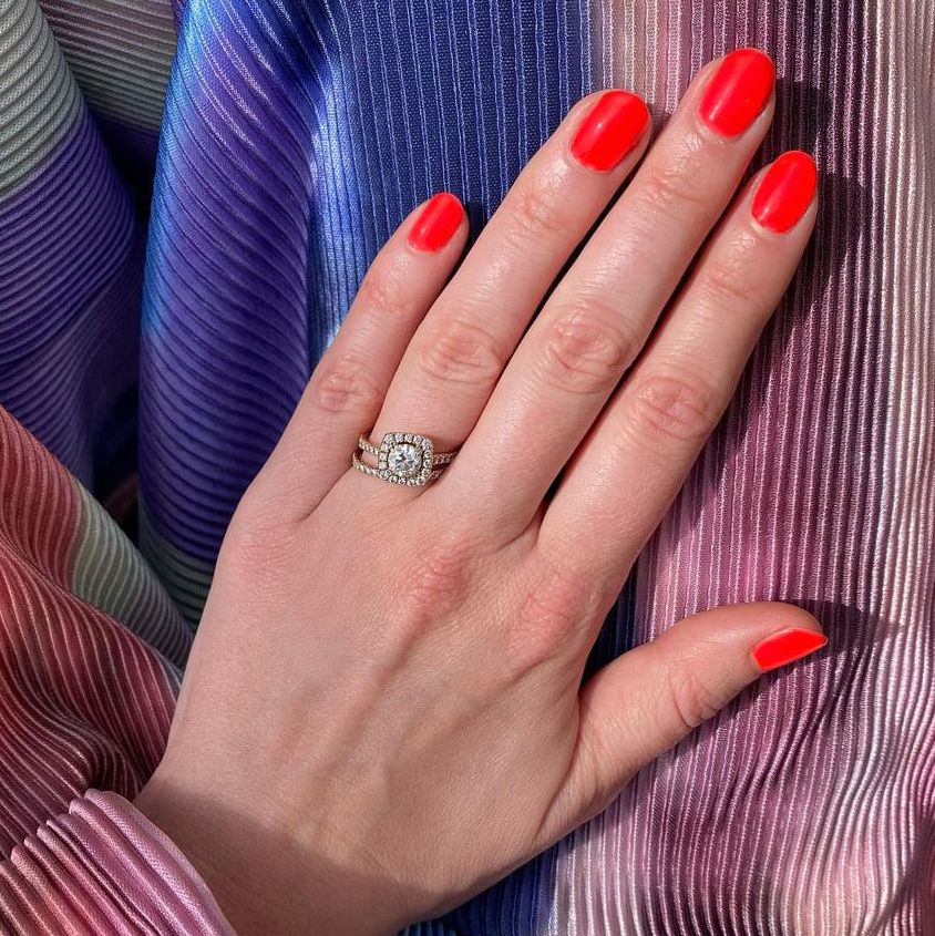 Main avec ongles rouges, portant une bague. Le fond est un matériau coloré et plié.